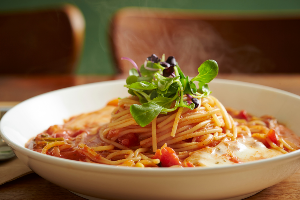 twirling spaghetti with tomato and green herbs in a bowl